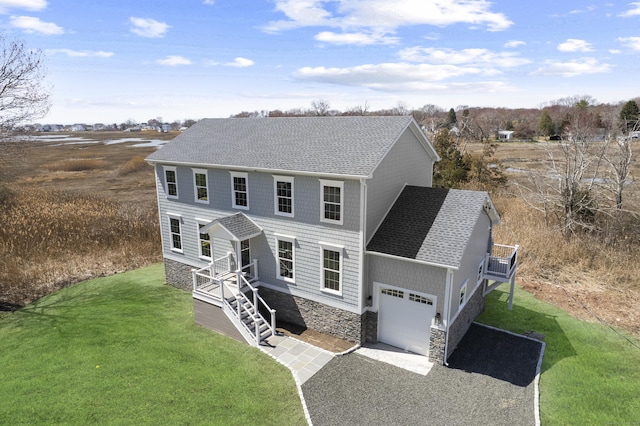 colonial-style house featuring a front lawn, driveway, roof with shingles, and a garage