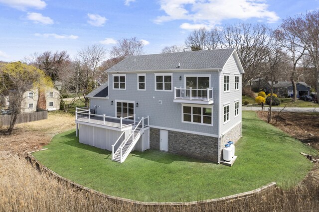back of house featuring a lawn, stone siding, a wooden deck, roof with shingles, and stairs