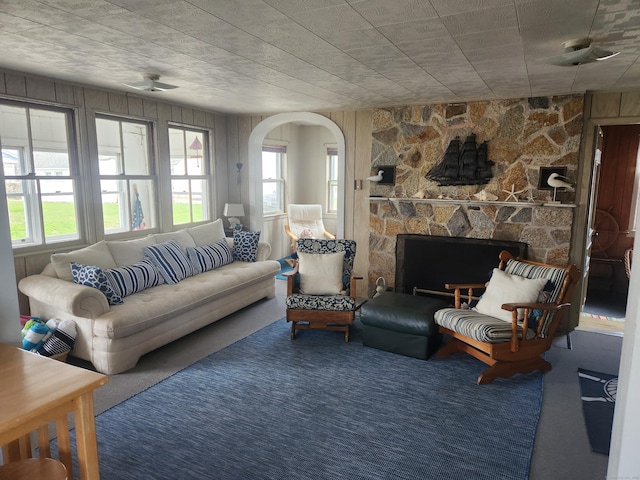 carpeted living room with arched walkways and a stone fireplace