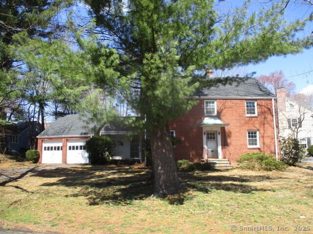 colonial-style house with brick siding, an attached garage, and a chimney