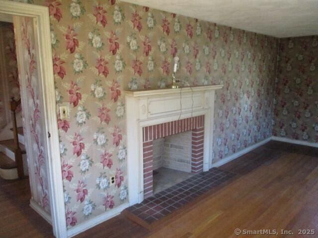 interior details with a fireplace, baseboards, wallpapered walls, and wood finished floors