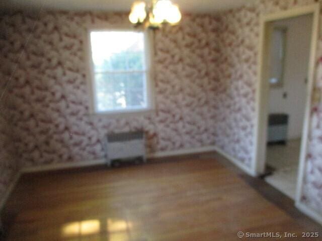 empty room featuring radiator, an inviting chandelier, wood finished floors, wallpapered walls, and baseboards