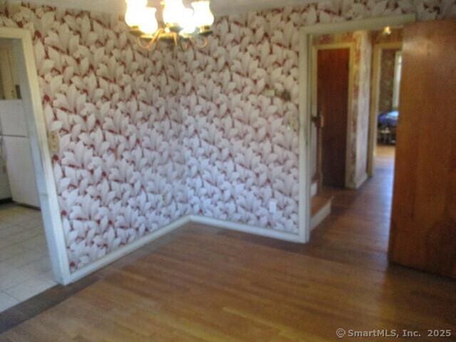 spare room featuring a notable chandelier, wood finished floors, and wallpapered walls