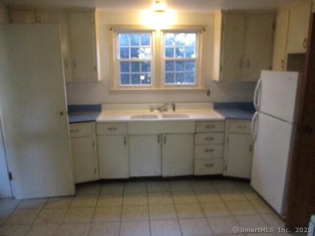 kitchen featuring light countertops, light tile patterned floors, a sink, and freestanding refrigerator