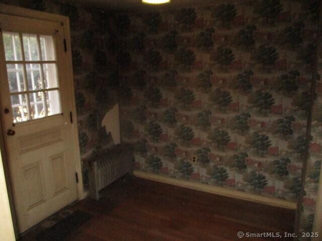 doorway to outside with a healthy amount of sunlight, wood finished floors, wallpapered walls, and radiator heating unit