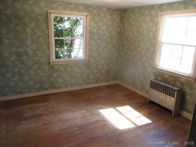 spare room featuring radiator, wood finished floors, and wallpapered walls