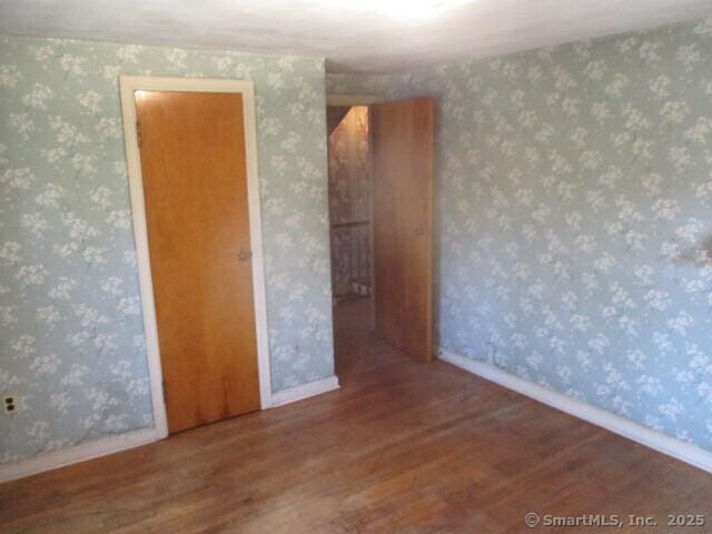 empty room with wallpapered walls, wood finished floors, and baseboards
