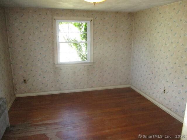spare room with baseboards, wood finished floors, and wallpapered walls