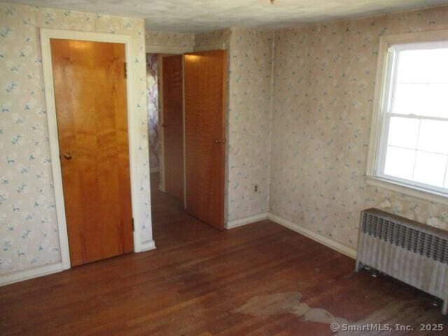 unfurnished room featuring radiator, plenty of natural light, wood finished floors, and wallpapered walls