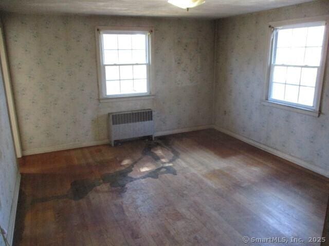 unfurnished room featuring wallpapered walls, radiator heating unit, baseboards, and wood finished floors