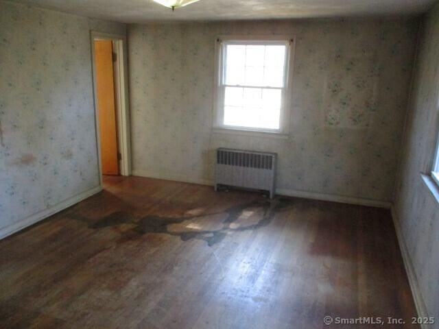 empty room with radiator heating unit, baseboards, wallpapered walls, and wood finished floors