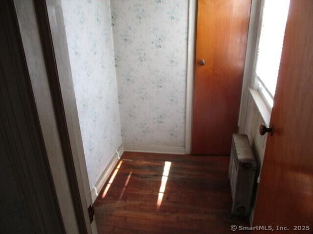 corridor featuring baseboards, radiator, wood finished floors, and wallpapered walls