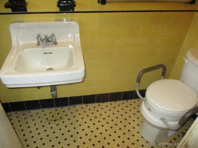 half bath with tile walls, a sink, and toilet