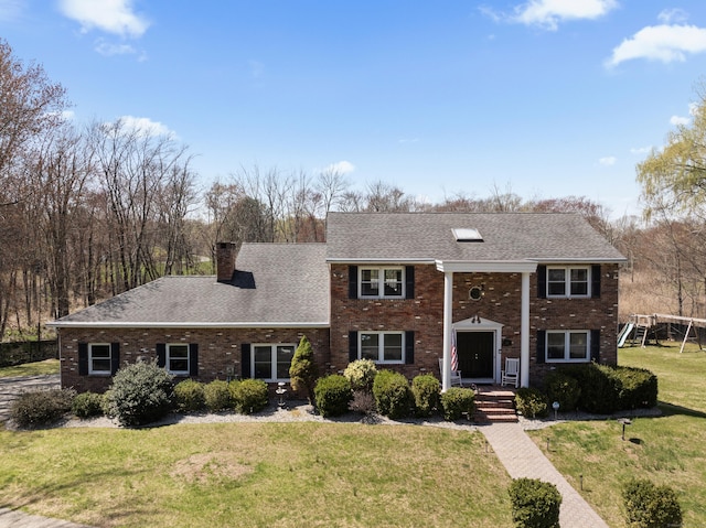 greek revival inspired property featuring a chimney, brick siding, a front yard, and roof with shingles