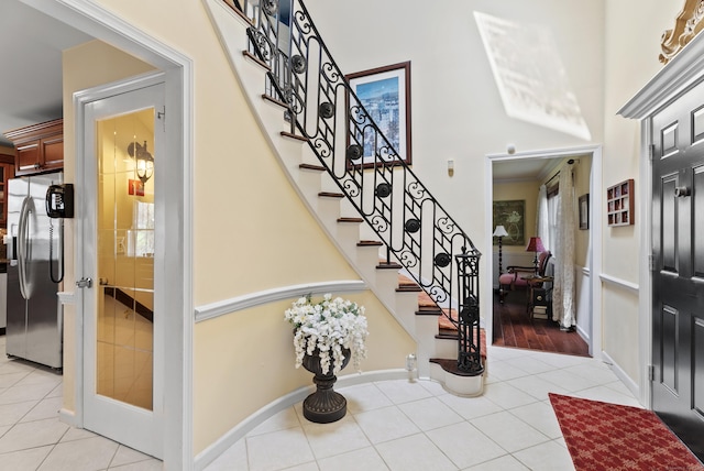 foyer with baseboards, light tile patterned floors, stairs, and a towering ceiling