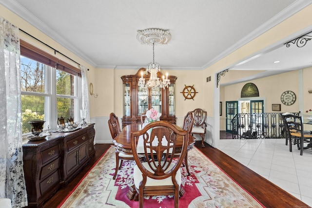 dining space with wood finished floors, an inviting chandelier, a wainscoted wall, visible vents, and crown molding
