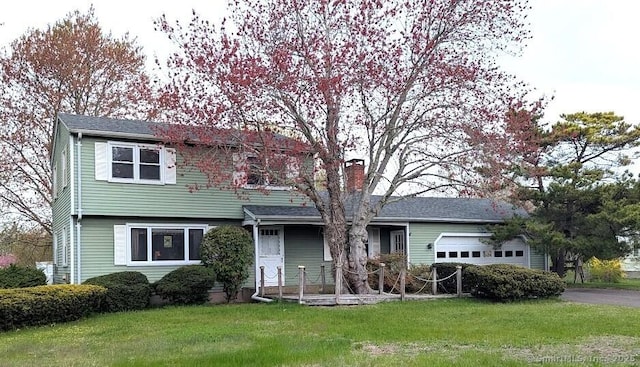 view of front facade with an attached garage, aphalt driveway, a chimney, and a front yard