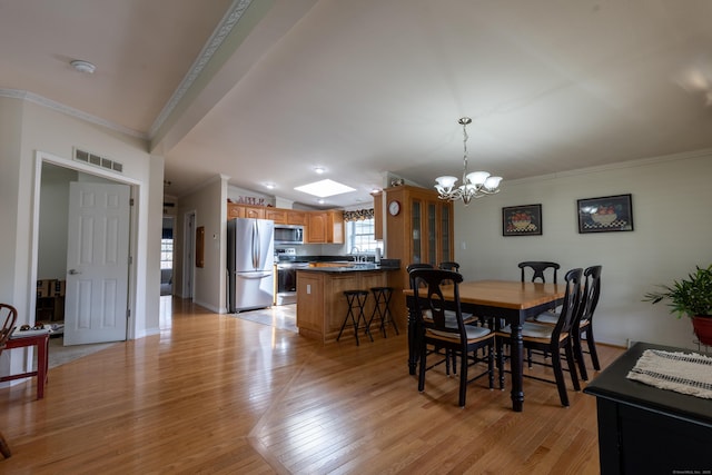 dining area with crown molding, a notable chandelier, light wood finished floors, and visible vents
