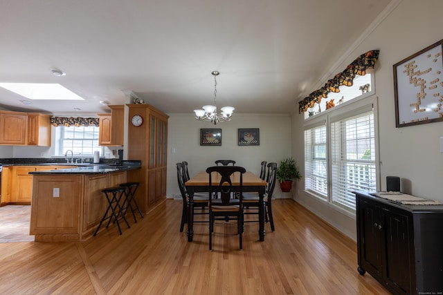 dining space featuring crown molding, baseboards, light wood-type flooring, a chandelier, and a skylight