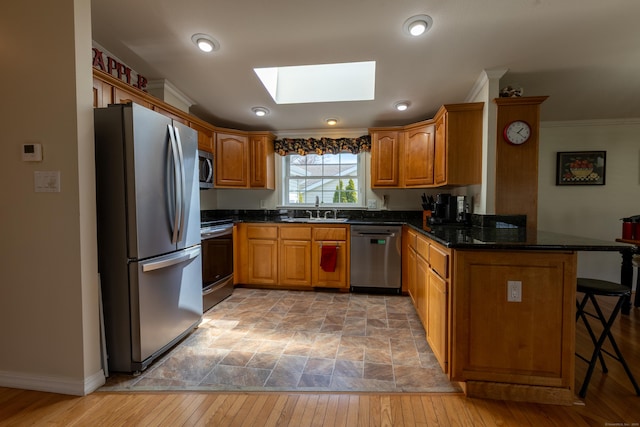 kitchen with appliances with stainless steel finishes, a sink, a peninsula, a kitchen bar, and a skylight