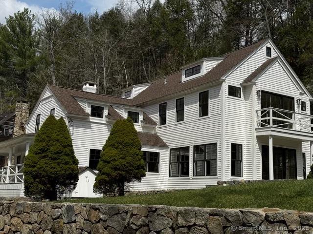 view of front facade with a chimney, a balcony, and a shingled roof