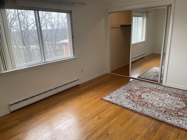 273 Queen St Apt 15E, Southington, CT 06489 - unfurnished bedroom featuring baseboard heating, a baseboard heating unit, wood finished floors, and a closet