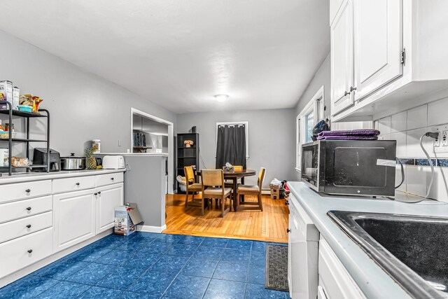 kitchen featuring white dishwasher, light countertops, a sink, and white cabinetry