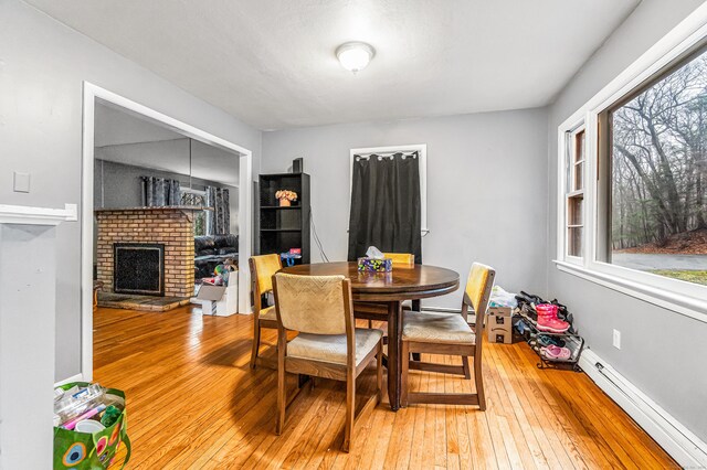 dining area featuring a baseboard radiator, light wood-style flooring, and a fireplace