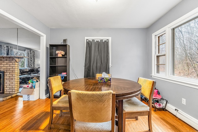 dining area with a fireplace, hardwood / wood-style floors, a healthy amount of sunlight, and baseboard heating