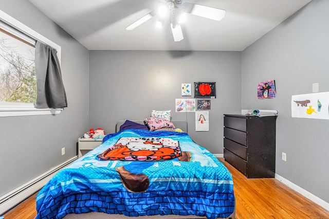 bedroom featuring a baseboard heating unit, wood finished floors, baseboards, and ceiling fan