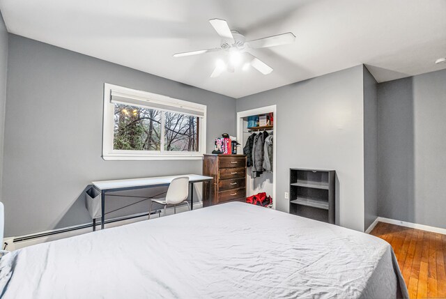 bedroom with a baseboard radiator, a ceiling fan, a closet, wood-type flooring, and baseboards