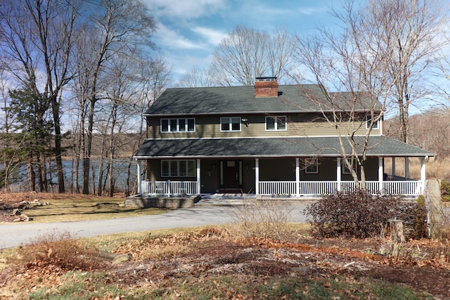 farmhouse-style home featuring roof with shingles, a porch, and a chimney