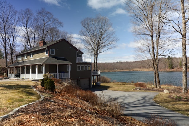 exterior space featuring roof with shingles, a chimney, a garage, aphalt driveway, and a water view