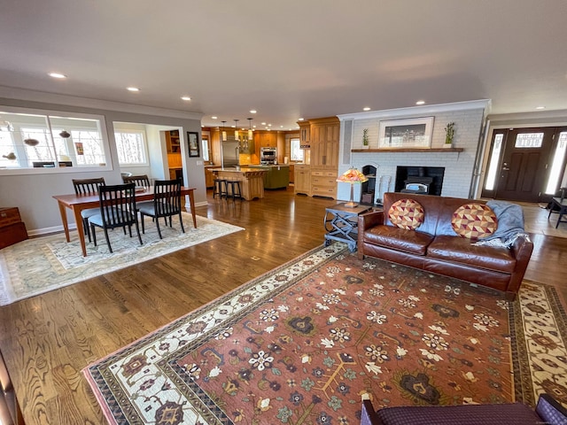 living area with dark wood-type flooring, crown molding, a brick fireplace, and a wealth of natural light