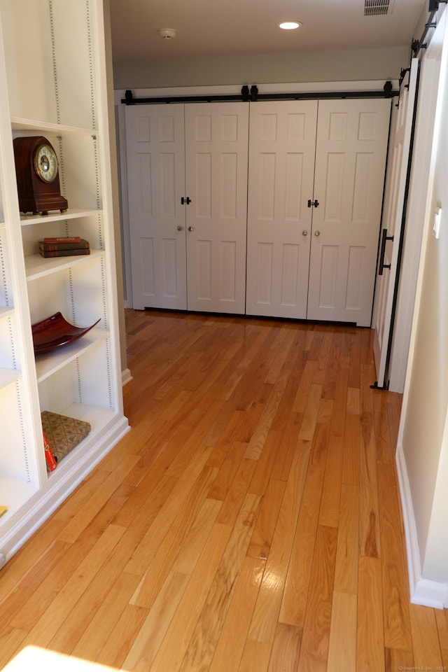 hallway with light wood-style floors, recessed lighting, visible vents, and a barn door