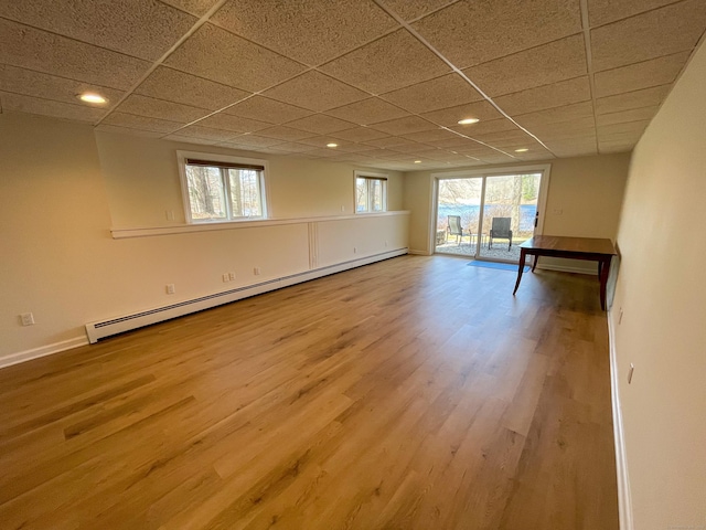 interior space featuring baseboards, a baseboard radiator, recessed lighting, wood finished floors, and a drop ceiling