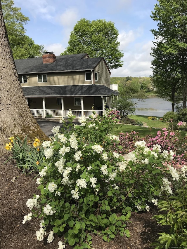 exterior space with a water view, roof with shingles, a porch, and a chimney