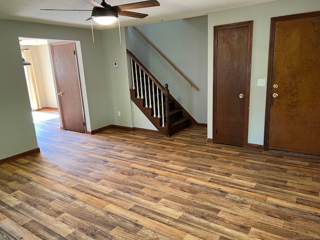 unfurnished living room featuring wood finished floors, a ceiling fan, stairs, and baseboards