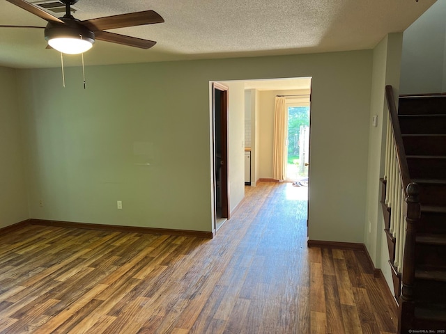 empty room with wood finished floors, ceiling fan, stairway, baseboards, and a textured ceiling