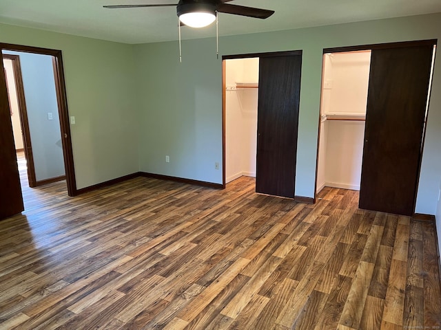 unfurnished bedroom featuring dark wood-style floors, baseboards, ceiling fan, and multiple closets