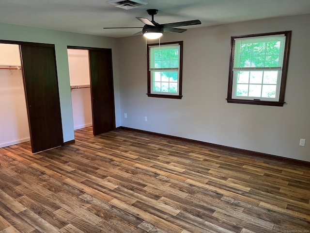 unfurnished bedroom featuring dark wood-style flooring, baseboards, multiple closets, and ceiling fan