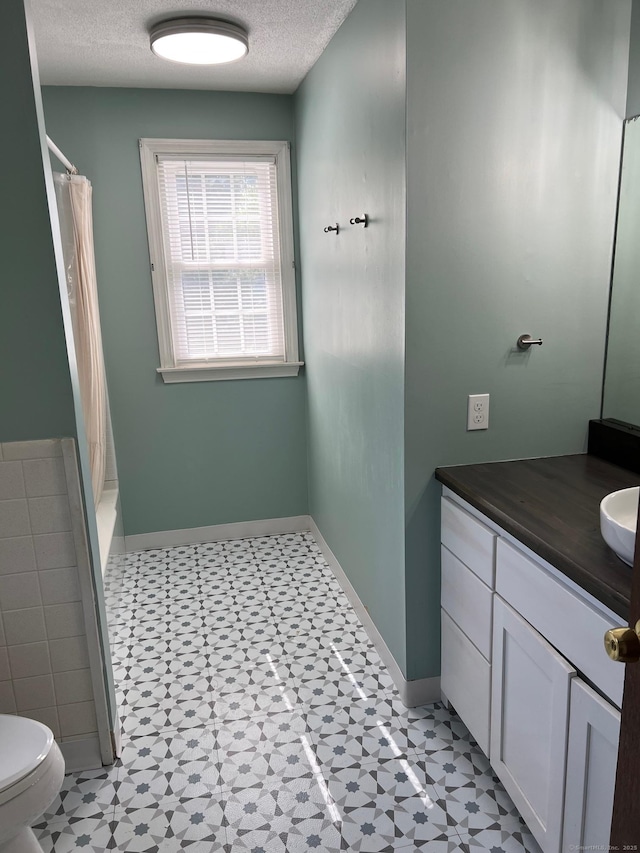bathroom with vanity, a textured ceiling, toilet, baseboards, and tile patterned floors