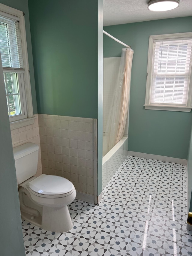 bathroom featuring toilet, tile walls, tile patterned floors, shower / tub combo, and a wainscoted wall