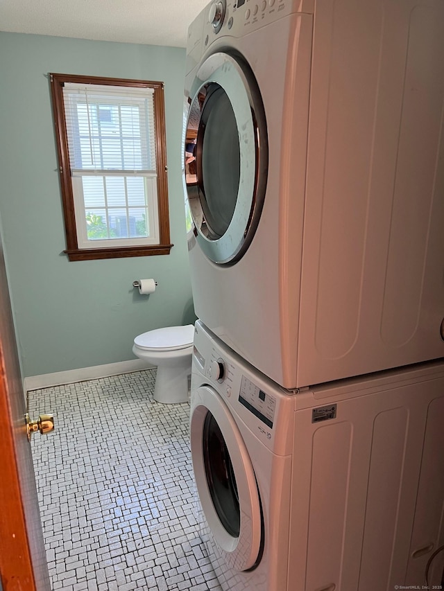washroom with stacked washer / drying machine and baseboards