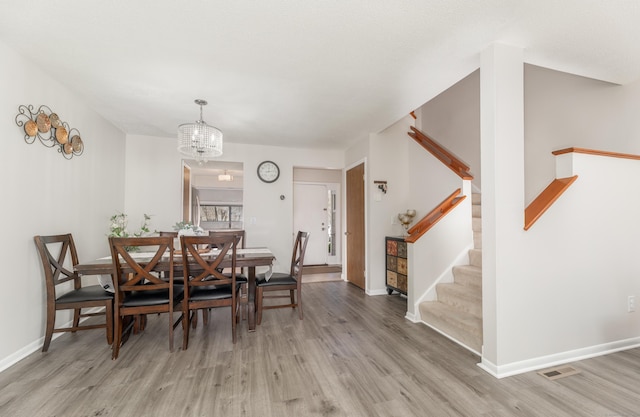 dining space with a chandelier, light wood finished floors, visible vents, and stairway