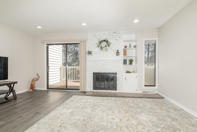 living room with wood finished floors, baseboards, visible vents, and a brick fireplace