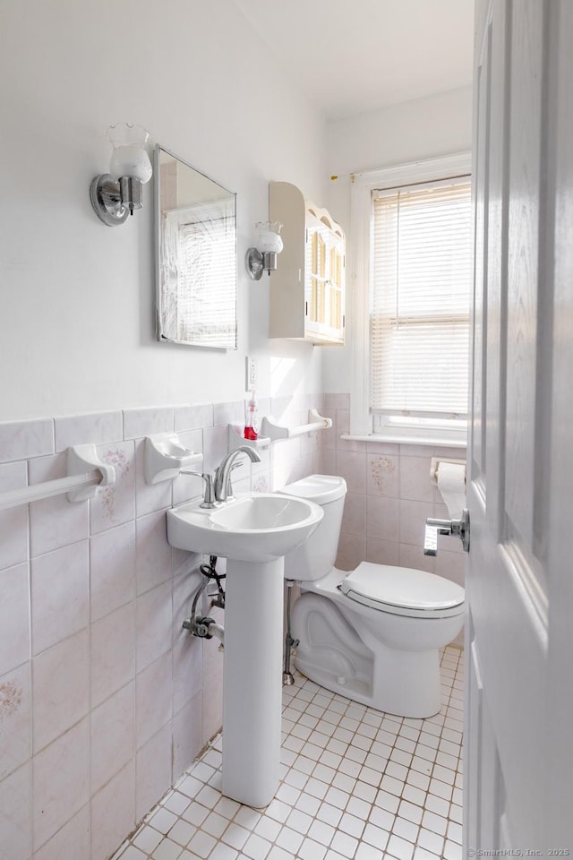 half bath featuring toilet, tile patterned floors, tile walls, and a wainscoted wall