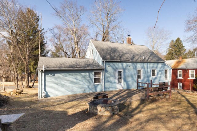 rear view of property featuring a fire pit, a chimney, and a shingled roof