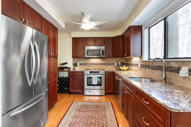 kitchen featuring a sink, appliances with stainless steel finishes, light stone counters, and light wood finished floors