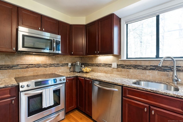 kitchen featuring a sink, light wood-style floors, stainless steel appliances, backsplash, and light stone counters